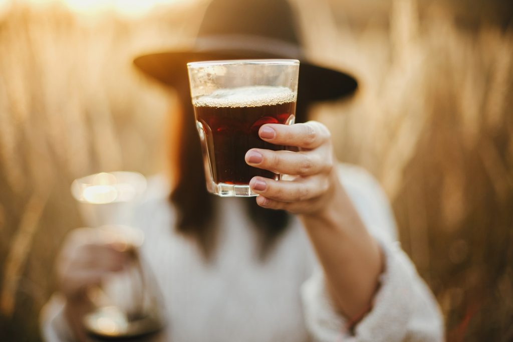 Hipster woman holding hot coffee and glass cup on background of rural herbs
